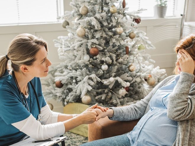 A woman looking distressed with a health care worker holding her hand in front of a christmas tree. 